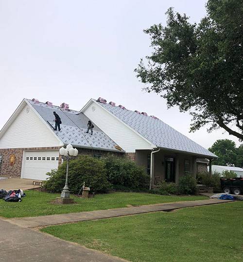 Roofers working on a residential roof replacement, installing new materials on a suburban home under cloudy skies.