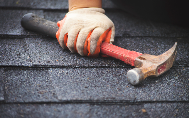 A Jenkins Roofing employee holding a hammer on a freshly shingled roof.